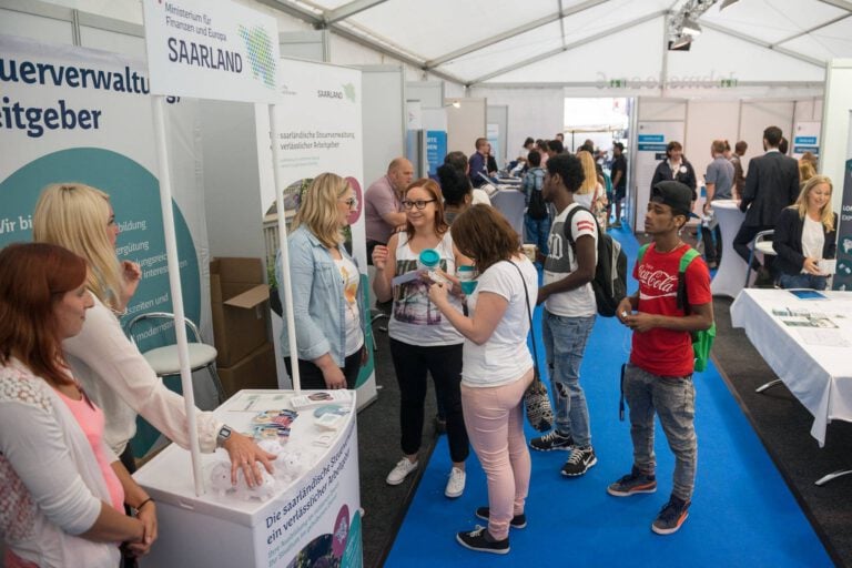 Menschen bei einer Outdoor-Jobmesse im Zelt, Informationsstände im Hintergrund.