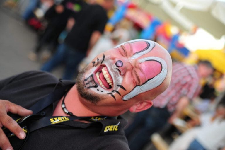Mensch mit bunter Clownmaske bei Firmenweihnachtsmarkt.