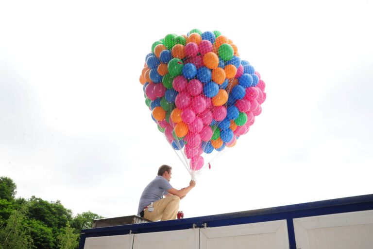 Mann hält bunte Ballons auf einem Dach bei Sonnenlicht.
