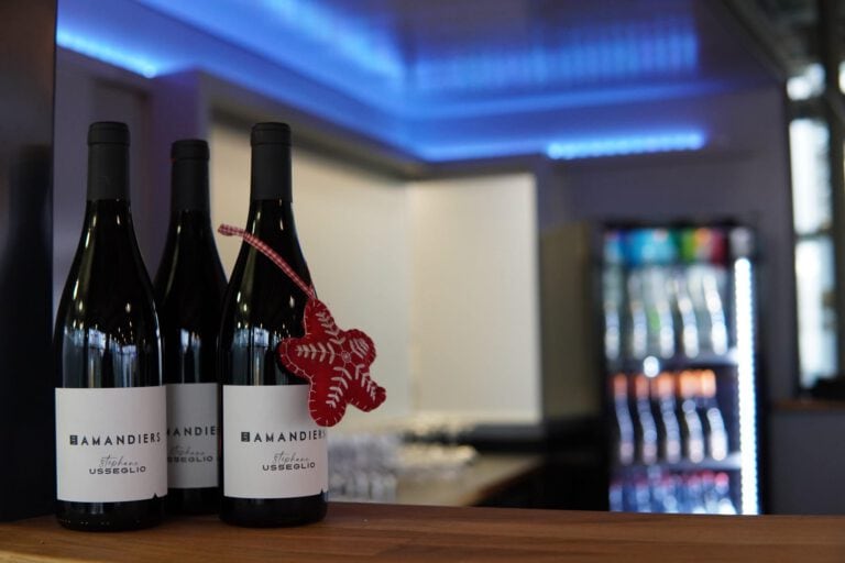 Drei Weinflaschen mit Weihnachtsanhänger auf einer Bar im Hintergrund.
