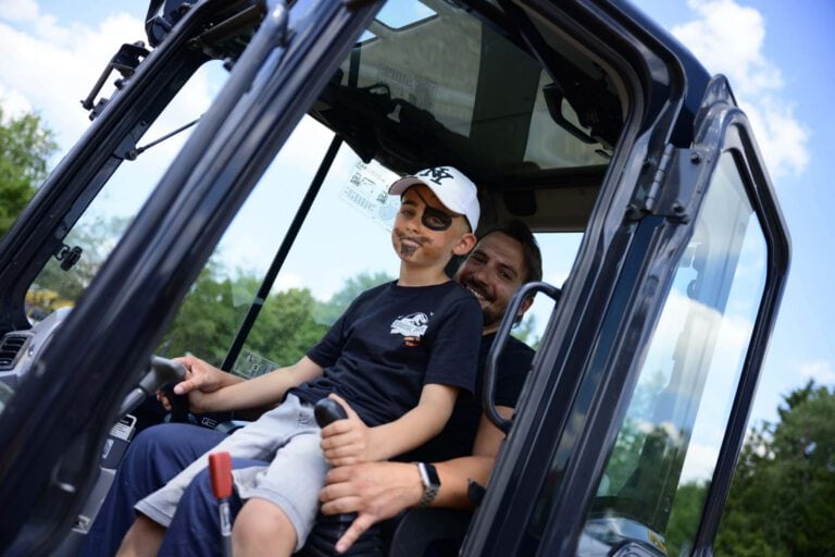 Kind und Erwachsener im Traktor, lachend bei 100-jährigem Jubiläum.