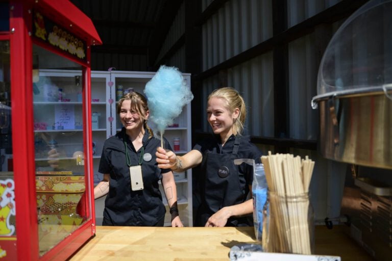 Zwei junge Frauen bei einem Sommerfest mit Zuckerwatte, fröhlich und lachend.