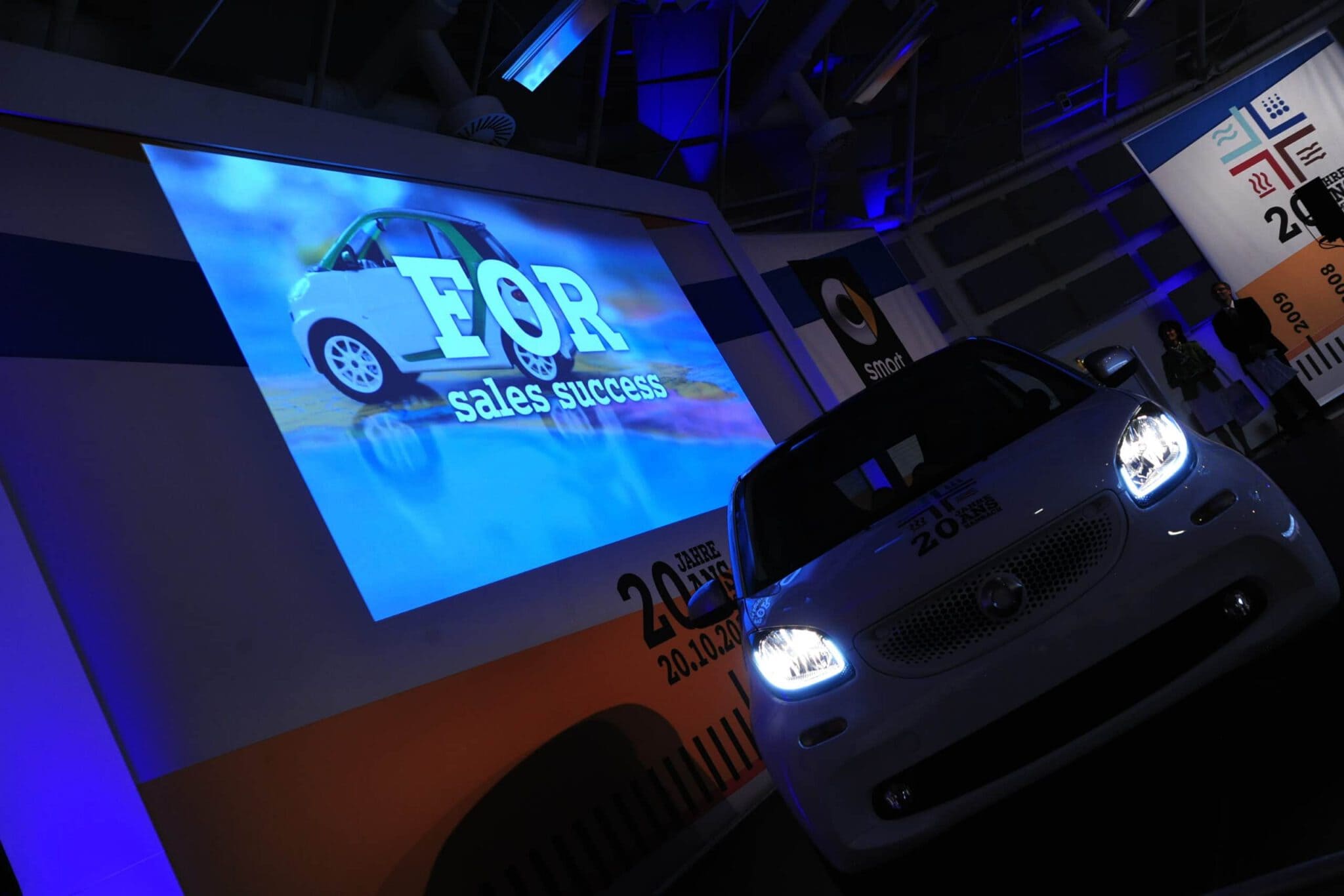 Elektrisches Auto bei Firmenveranstaltung mit Präsentation im Hintergrund.