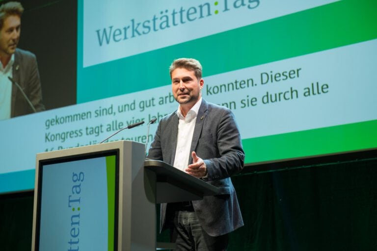 Mann spricht bei Werkstätten:Tag 2022 vor Publikum und Bühne.