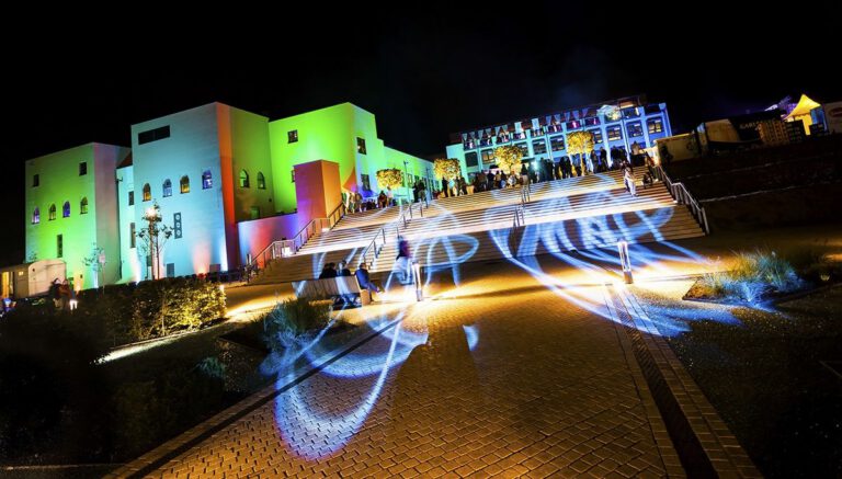 Bunt beleuchtete PURA Erlebnismanufaktur bei Nacht mit Lichtprojektionen.