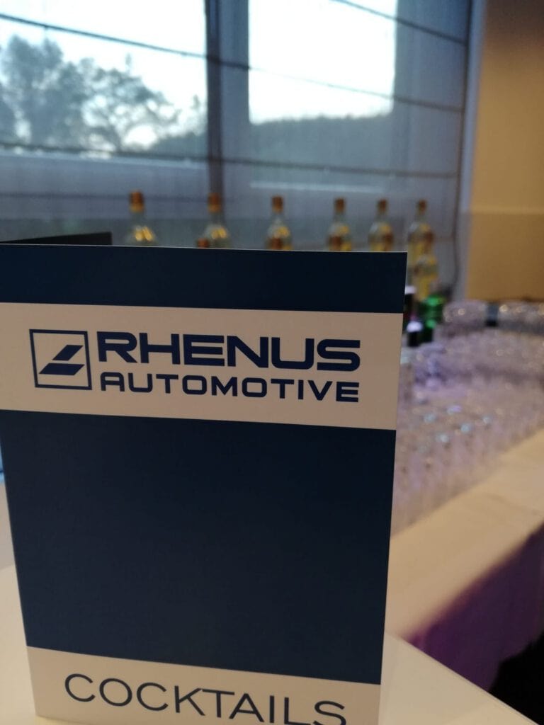 Rhenus Automotive Logo bei PURA Erlebnismanufaktur mit Cocktails im Hintergrund.