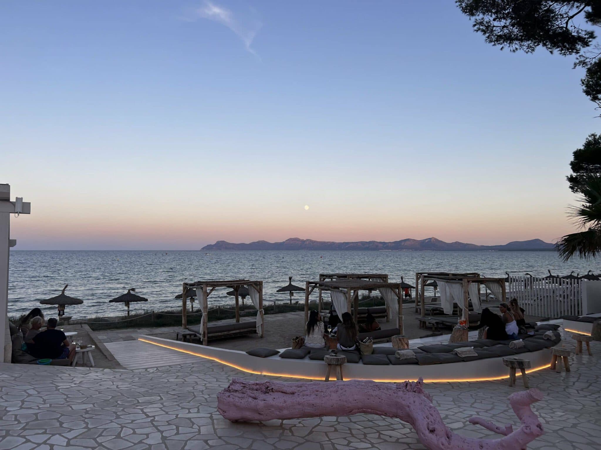 Strand mit Sonnenuntergang, Liegestühlen und Palmen bei PURA Erlebnismanufaktur.